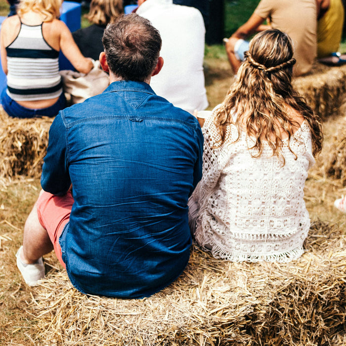 Couple sitting on a hay bale at a festival with children playing in background