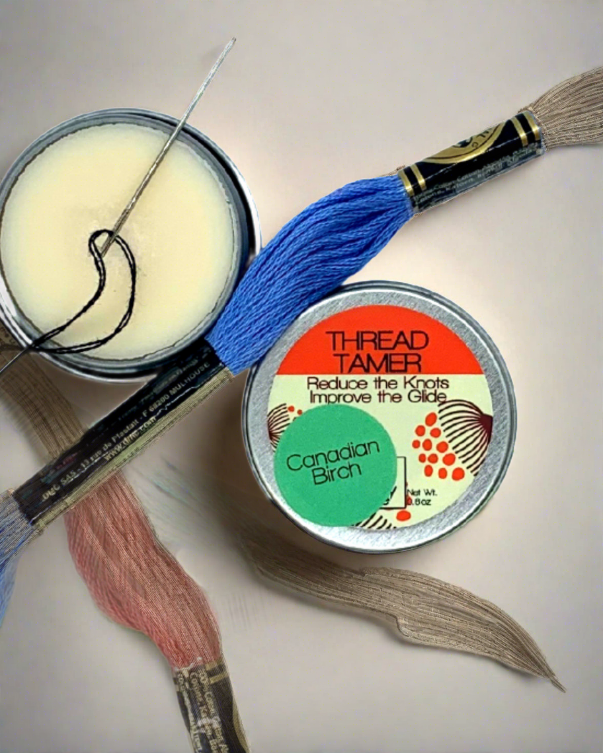 Small open can of solid beeswax and plant based material with needed and colored thread